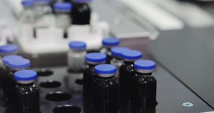 Automated gripper inserts black medicine vials into designated tray openings. Robotic system repeats accurate placement during pharmaceutical line processing