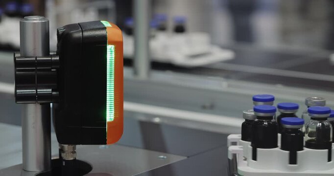 Machine vision scanner inspects medicine vials on automated line. Optical system checks liquid containers identifying defects before further processing