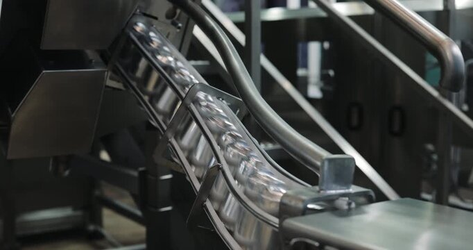 Enclosed conveyor carries empty metal cans through inclined factory section. Automated transport system directs containers toward downstream processing stage