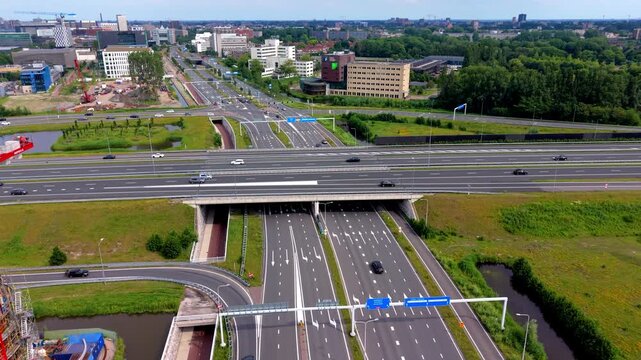 High angle horizontal aerial drone video clip of highway junction, traffic, red crane, industrial gasometer, and cityscape in Leiden, South Holland, Netherlands, West Europe