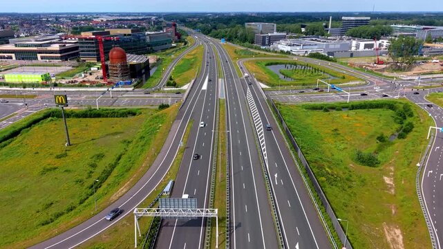 High angle horizontal aerial drone video clip of highway junction, traffic, industrial gasometer, office buildings, and cityscape in Leiden, South Holland, Netherlands, West Europe