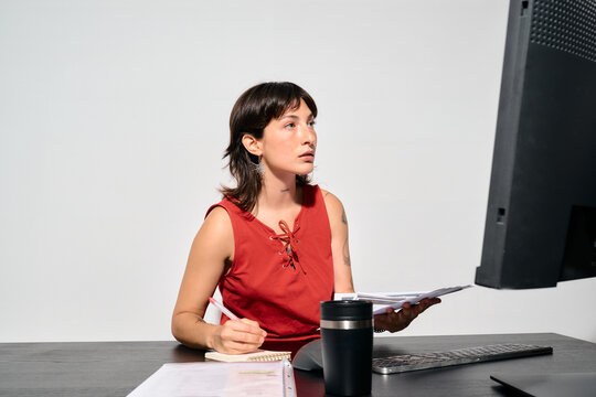 A focused woman works at her desk. She reviews documents while looking at her computer screen. 