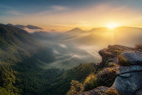 Golden sun rises over misty mountain peaks. Rugged cliffside frames the serene valley below. Vivid greens and soft grays define the natural beauty. Mist swirls between forested hills, adding mystery