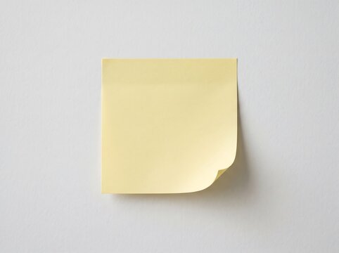 Yellow sticky note on white wall, blank adhesive paper for office reminders and messages