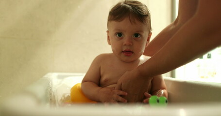 Fototapeta premium Bathing baby infant inside bathtub. Parent washing and cleaning toddler