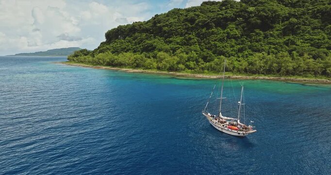 Travel to Tegua island in the Torres group, Vanuatu. Sailboat anchoring in calm turquoise water during a sunny day, showcasing a tropical paradise with lush green vegetation covering the shoreline