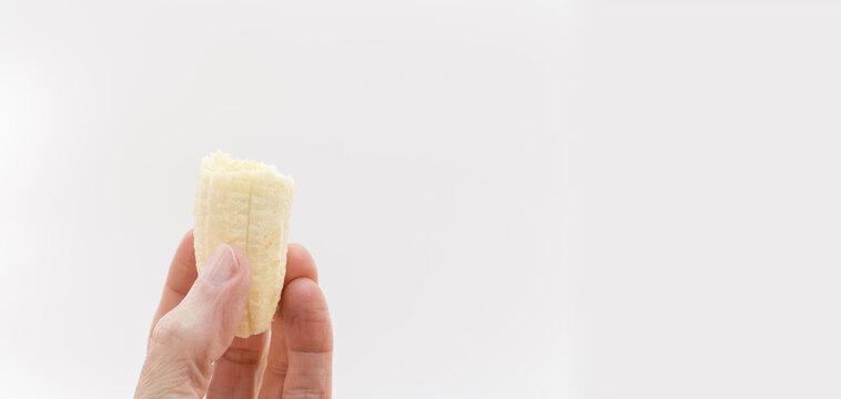 Parte di frutto di banana matura tenuto tra le dita di una mano primo piano su sfondo bianco con spazio per testo