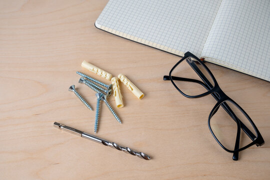 Glasses, notebook, screws, and colorful dowels on plywood