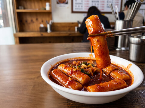 Metal chopsticks lifting thick Korean spicy rice cake Tteokbokki with dripping red sauce in local diner