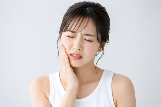 歯の痛みに悩み頬を押さえる若い日本人女性