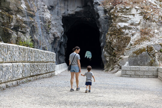 Mother And Young Son Walking Toward Dark Tunnel Entrance At Othello Tunnels In Hope, BC Canada