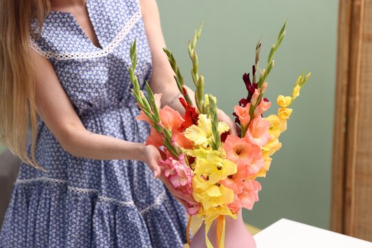 Woman with beautiful gladiolus flowers at home, closeup