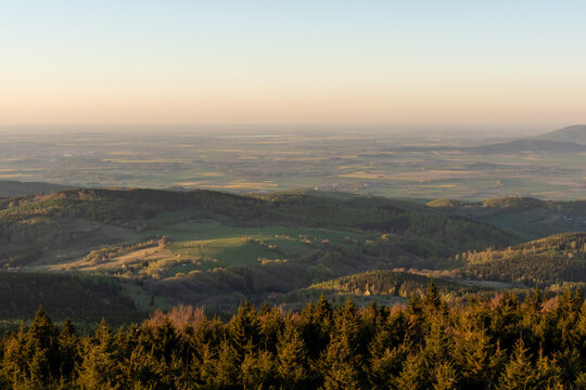 Expansive panoramic view of rural valley with green farmland, forests and distant settlements seen from high mountain viewpoint in soft golden hour light. Concept of agriculture, countryside