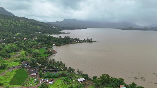 Expansive aerial drone view of scenic Pawna Lake reservoir surrounded by lush green hills under overcast monsoon sky⁠