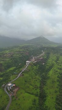 Vertical drone view of serene Pawna Lake with rolling green hills and foggy monsoon clouds in Maharashtra⁠