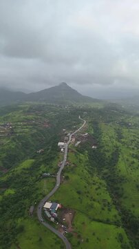 Vertical drone view of serene Pawna Lake with rolling green hills and foggy monsoon clouds in Maharashtra⁠