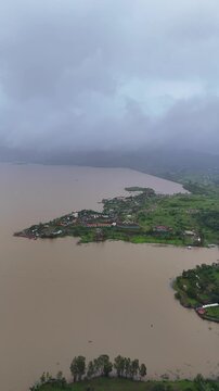 Vertical drone view of serene Pawna Lake with rolling green hills and foggy monsoon clouds in Maharashtra⁠