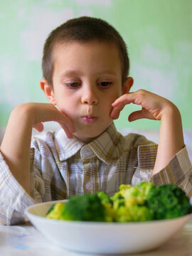 Picky boy staring unhappily at bowl of green broccoli refusing to eat healthy vegetables