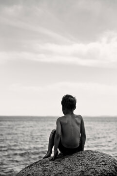 Rear view of a Boy in swimming trunks sitting on a rock by the sea on a summer day, Sweden