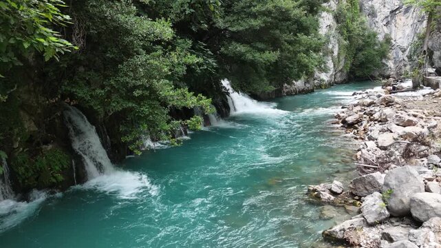 Cinematic view of a wild turquoise river flowing through a lush green rocky canyon.