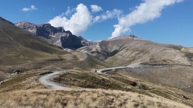 Cinematic shot of a winding dirt road cutting through a remote mountain landscape under a blue sky.