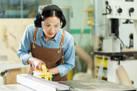 Female carpenter using table saw with safety gear in woodworking workshop