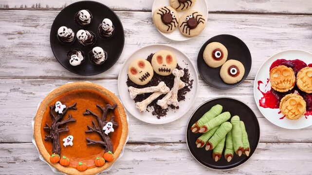 Fun Halloween dessert table scene over a white wood background. Stop motion animation table placement. Above view. Variety of cookies, cupcakes and pumpkin and apple tarts and pies.