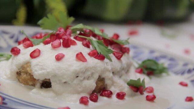 Elegant chile en nogada featuring a golden capeado chile, creamy walnut sauce, pomegranate, and parsley, beautifully presented on Talavera pottery.