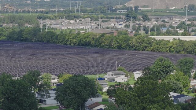 Drone aerial of large midwest field full of solar panels absorbing sunlight and sun light for green energy to fuel nearby Columbus, Ohio data centers on south side of town by middle class neighborhood
