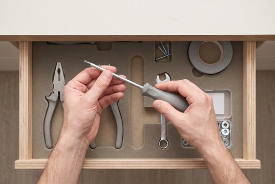 Hands holding a screwdriver above an organized drawer containing various tools