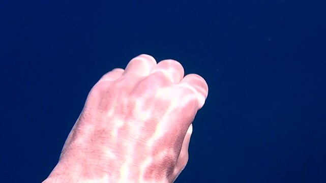 Underwater human hand making grabbing gestures with light ripple patterns on back