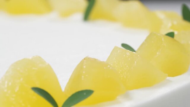 A macro, shallow-depth-of-field shot showcasing the decorative topping of a delicious homemade fruit dessert. Vibrant, yellow diced pineapple chunks are neatly arranged on a smooth, white whipped crea