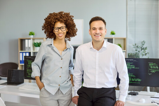 Programmers colleagues show teamwork in office, smiling. Developers and coders by computer screens with code, showing modern technology and workplace. Clear concept of collaborative tech teams.