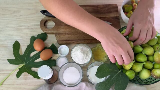 Top view of a woman preparing ingredients for baking, fresh green figs in a bowl, eggs and flour on a wooden table, rustic kitchen atmosphere