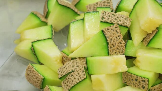 close-up shot of juicy, fresh muskmelon slices cut into bite-sized pieces and served in a clear glass bowl, showcasing the vibrant green rind and pale yellow flesh.