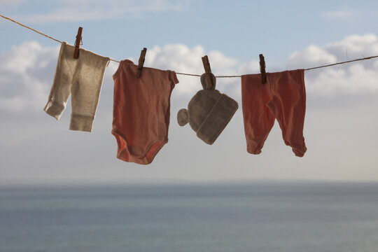  baby clothing hanging on an outdoor clothesline to air dry naturally with a scenic ocean and sky background. Concept of eco-friendly laundry, energy-saving habits, and peaceful seaside lifestyle.
