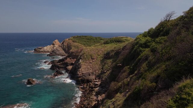 4K drone footage flying smoothly forward at low altitude over the sea in Oaxaca, Mexico, with waves breaking against rocks below as coastal vegetation appears on the right and Punta Cometa 