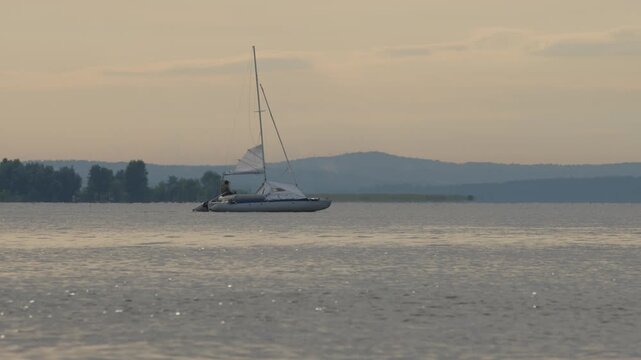 Sailing boat moves on the lake with during sunset