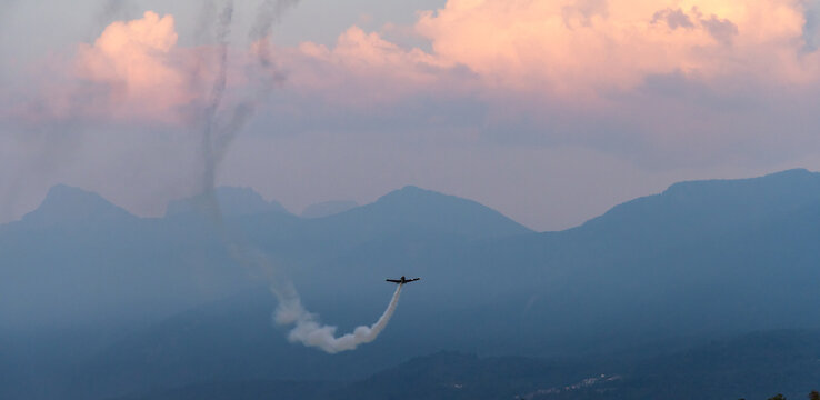 Solo Aerobatic Plane Leaving Smoke Trail Over Mountain Landscape At Sunset In Chilliwack BC