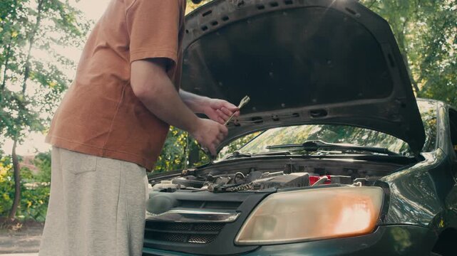 Person tightening engine component with wrench under open hood during emergency roadside car repair. Vehicle maintenance happens after unexpected breakdown.