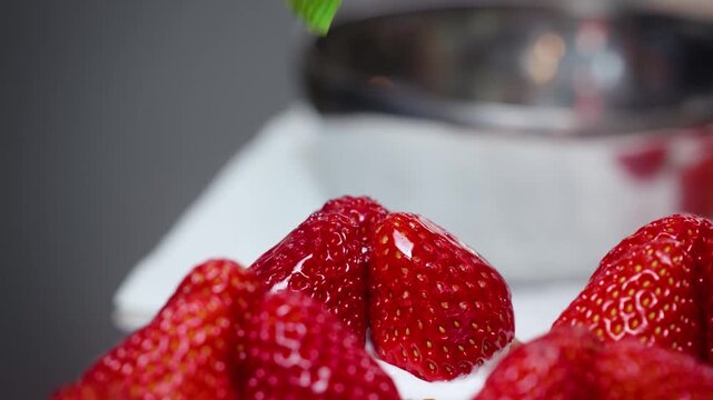 Close-up shot of a green silicone pastry brush applying a glossy sugar glaze or gelatin over fresh, vibrant red strawberries on top of a delicious cake or dessert.