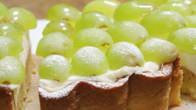 close-up shot of a delicious fruit dessert featuring a crisp pastry tart shell filled with creamy custard or pastry cream, topped with fresh, juicy green grapes lightly dusted with powdered sugar.