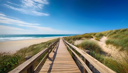 Fototapeta premium A Wooden Boardwalk Leads Through Grassy Sand Dunes To A Bright Ocean Beach Under Blue Sky Suited For Travel Tourism Vacation And Coastal Lifestyle Promotions