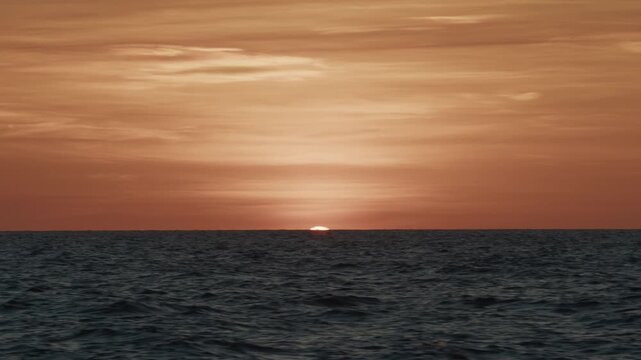 Sunset in the open sea. Sun hides in the sea as seen from the moving sailing vessel.