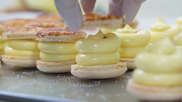 Close-up video footage of a pastry chef wearing a white glove assembling gourmet French cr&Atilde;&fnof;&Acirc;&uml;me br&Atilde;&fnof;&Acirc;&raquo;l&Atilde;&fnof;&Acirc;&copy;e macarons, placing the delicate almond cookie shell topped with caramelized sugar onto a th