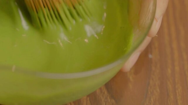 Close-up of traditional matcha preparation as green tea powder is whisked in a bowl with a bamboo whisk, showcasing authentic Japanese tea culture.