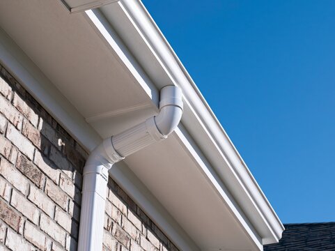 White rain gutter system on a brick house with a clear blue sky above, showing excellent drainage and home exterior design.