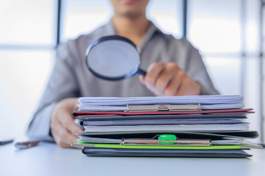 Auditor Using Magnifying Glass Over Stack of Documents to Inspecting or Auditing. Concept for Corporate Audit, Compliance Legal Document Review, or Investigating Corporate Fraud.