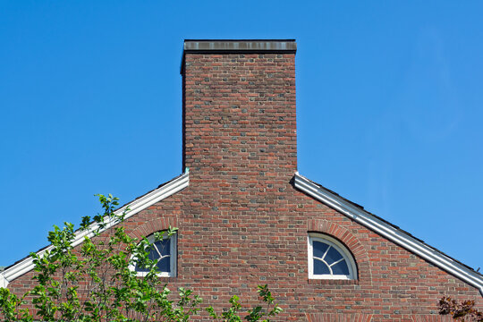 Massive brick exterior chimney and quarter round windows on a house gable in Boston