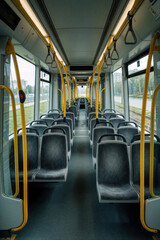 Fototapeta premium Empty tram interior shows rows of grey passenger seats and yellow safety handles. Modern public transport vehicle travels through city on a cloudy day.